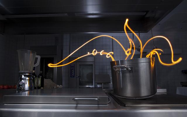 Orangefarbene Lichtzeichnung über einem Kochtopf in einer Großküche
