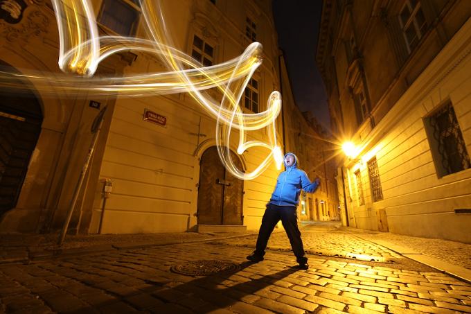 Person in a blue jacket drawing with light in an old-town alley at night