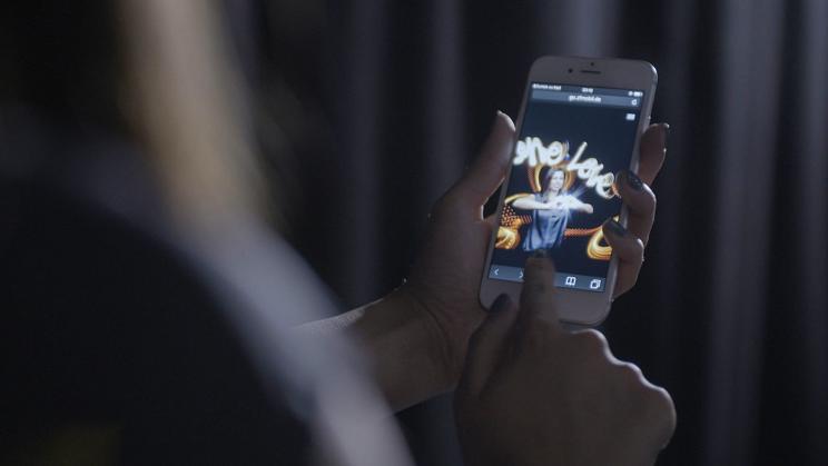 Hände halten ein Smartphone, auf dem Display ein Lichtbild mit Schriftzug