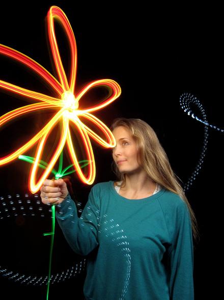 Frau hält eine mit orangefarbenem Licht gezeichnete Blume