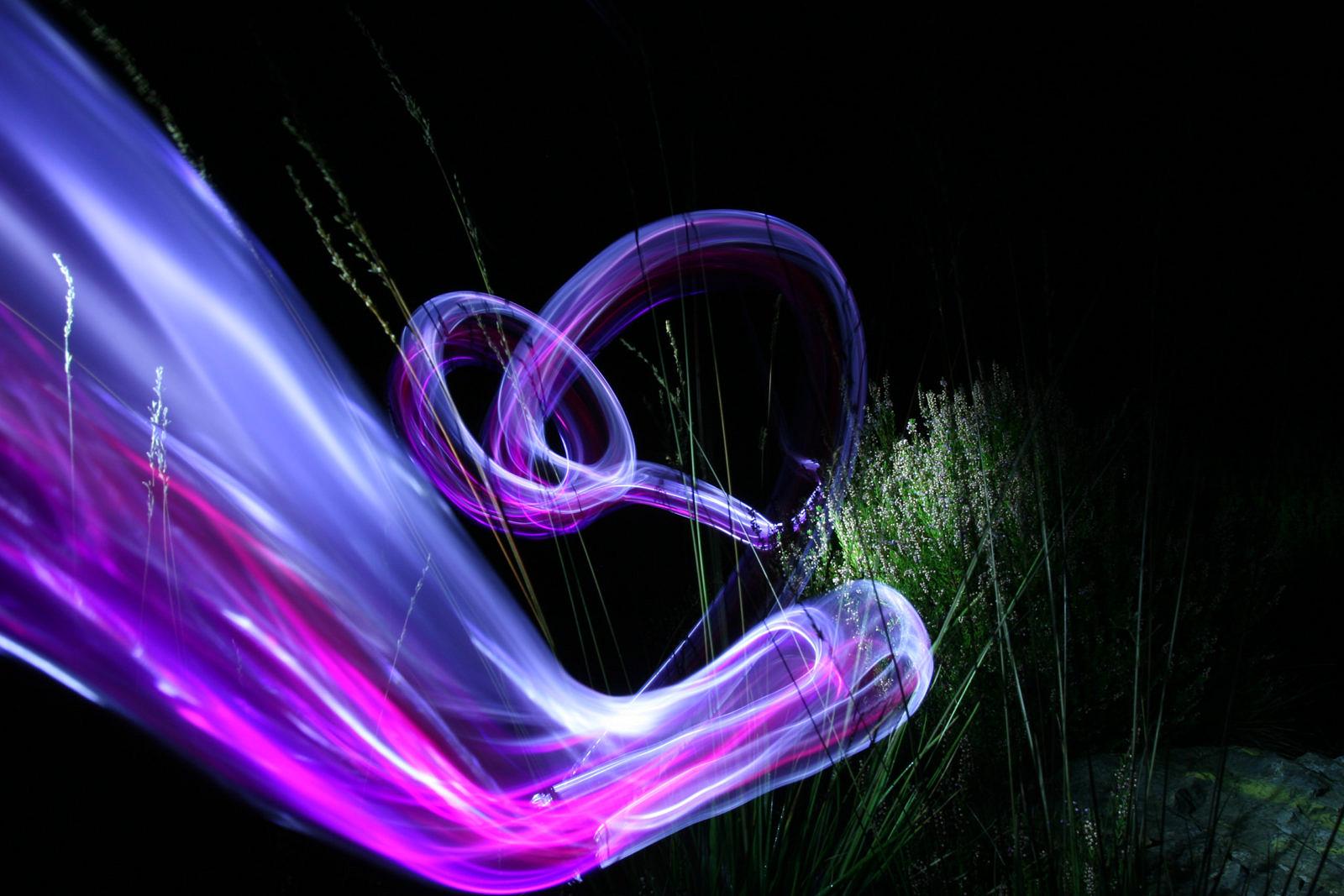 Sweeping violet and white light trail above grass at night