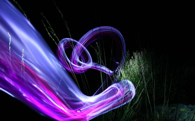 Violette und pinke Lichtschleife vor einer dunklen Wiese bei Nacht