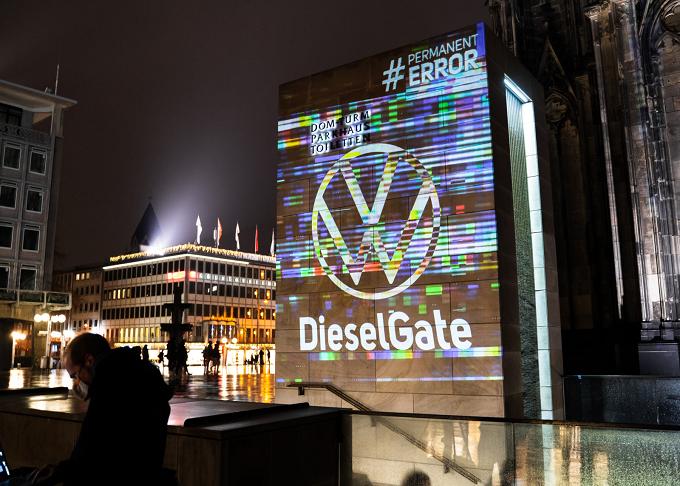 Fassade mit Projektion des VW-Logos und dem Schriftzug „DieselGate“ bei Nacht