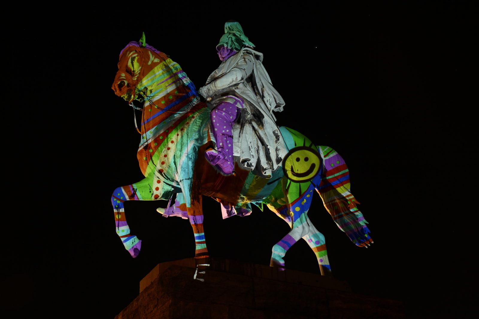 Reiterstandbild bei Nacht, mit bunten Mustern und einem Smiley bestrahlt