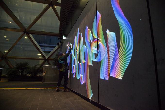 Person zeichnet an einer Wand mit bunten Lichtstreifen, Licht-Graffiti in Regenbogenfarben