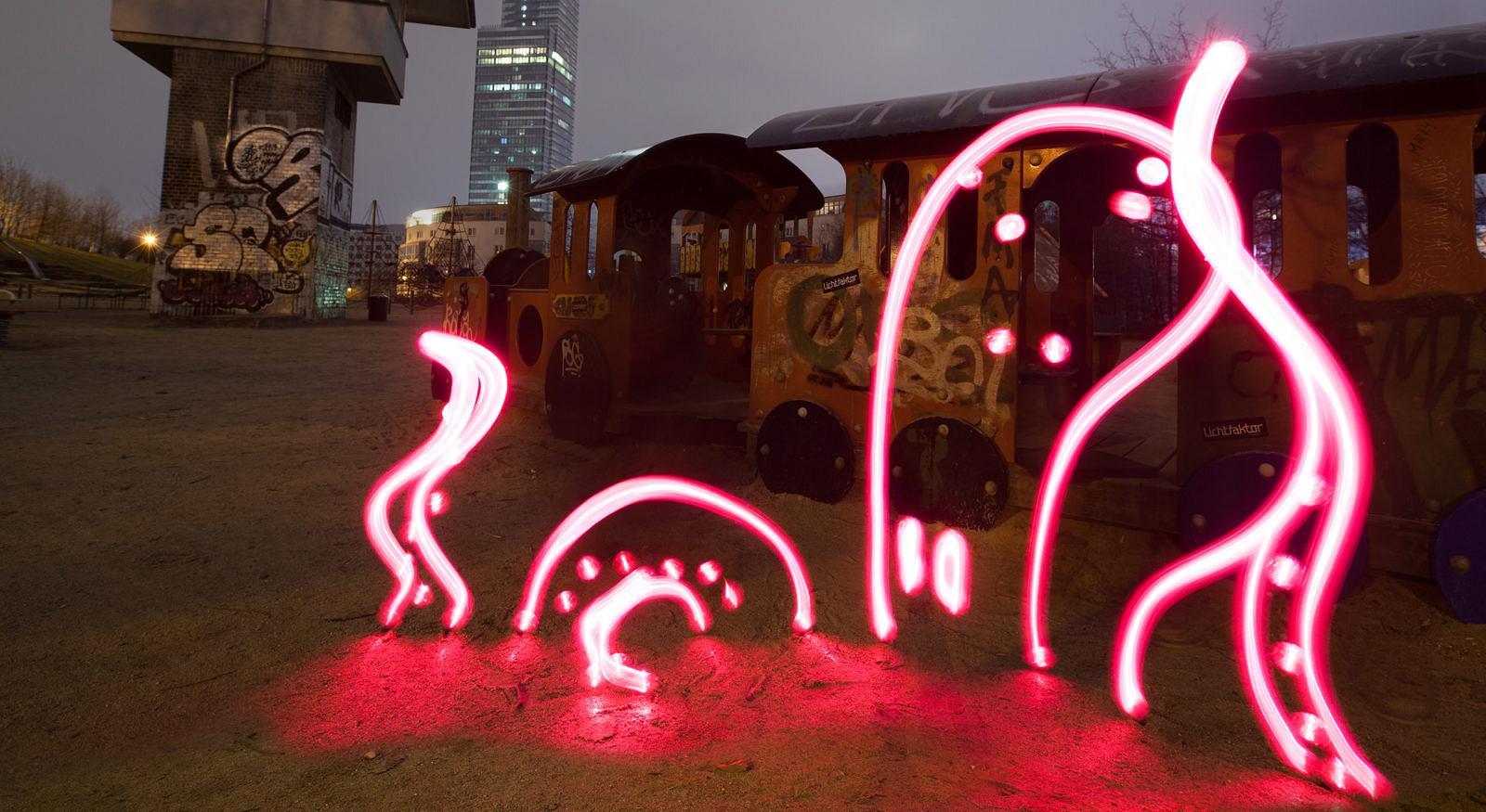 Pinke Lichtzeichnung eines Oktopus vor einem alten Spielplatzzug