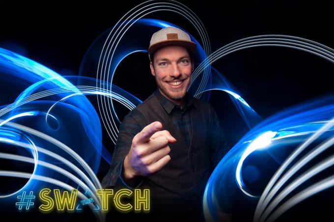 Mann mit Cap zeigt auf die Kamera, umgeben von blauen Lichtschleifen, unten der Schriftzug „#Swatch“