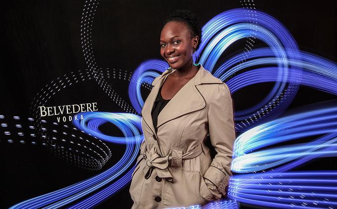 Frau im Trenchcoat vor blauen Lichtschleifen, dahinter der Schriftzug „Belvedere Vodka“