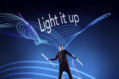 Performer mit Leuchtstäben vor einer blauen Lichtprojektion mit dem Schriftzug „Light it up“