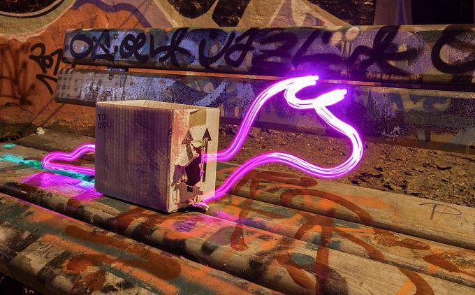 Pinke Lichtzeichnung auf einer mit Graffiti bedeckten Bank neben einem Schaltkasten