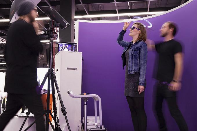 Fotostudio mit violettem Hintergrund, eine Frau und ein Mann in Bewegung, im Vordergrund eine Kamera auf einem Stativ