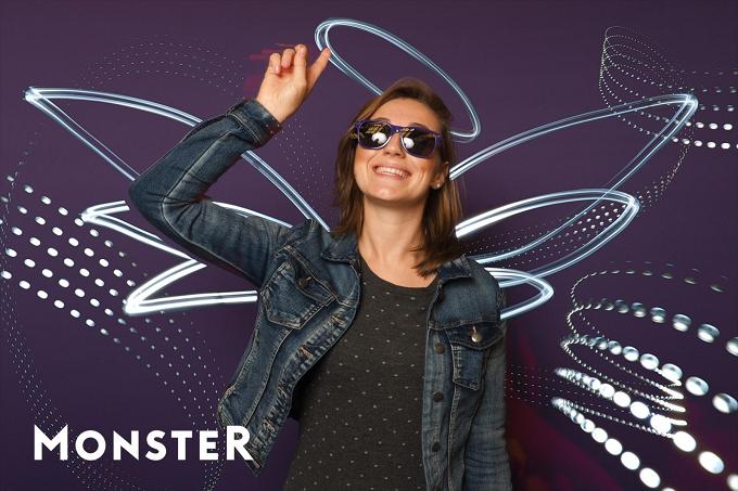 Frau mit Sonnenbrille tanzt vor violettem Hintergrund mit Lichtflügeln, unten der Schriftzug „Monster“