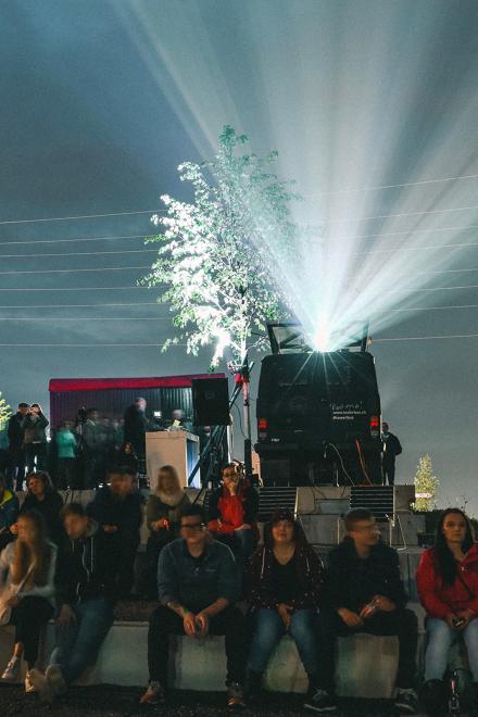 Zuschauer sitzen nachts vor einem Projektor, der Lichtstrahlen in den Himmel wirft