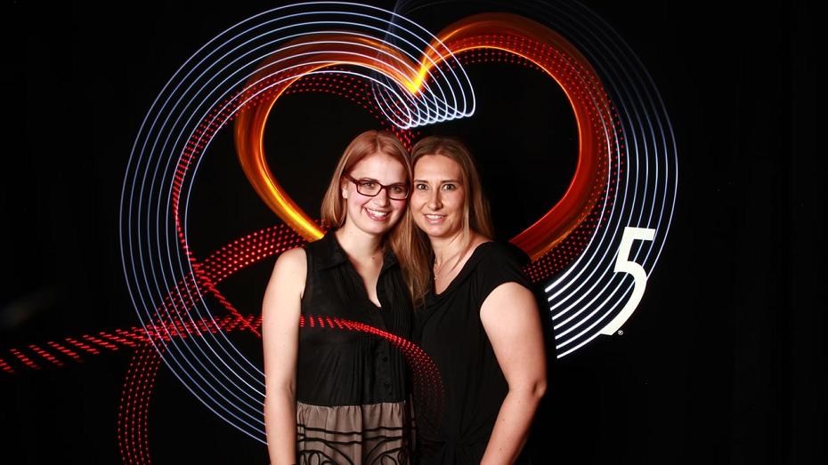 Zwei Frauen mit Brille vor einem Herz aus rotem und weißem Licht