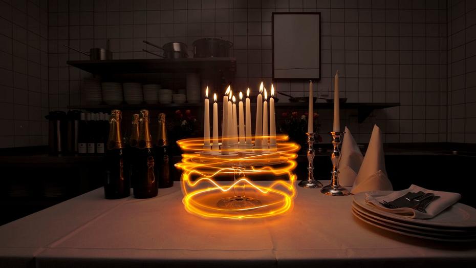 Torte mit Kerzen, umgeben von mit Licht gezeichneten Ringen, auf einem gedeckten Tisch