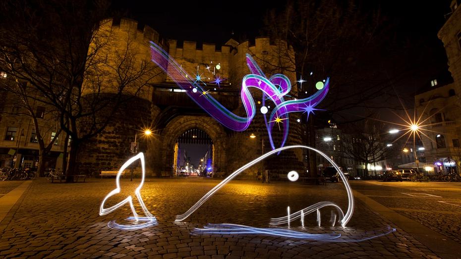 Mit Licht gezeichneter Wal vor einem alten Stadttor in Köln bei Nacht